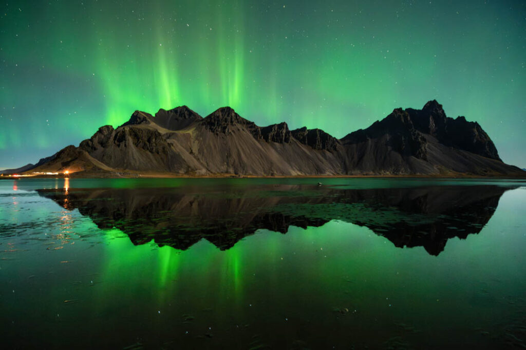 Grünes Polarlicht über Bergen spiegelt sich im stillen Wasser – Sinnbild für innere Klarheit und spirituelle Energie