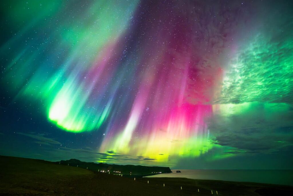 Farbenfrohes Polarlicht in Pink und Grün am Sternenhimmel über der Küste – Sinnbild für spirituelles Erwachen